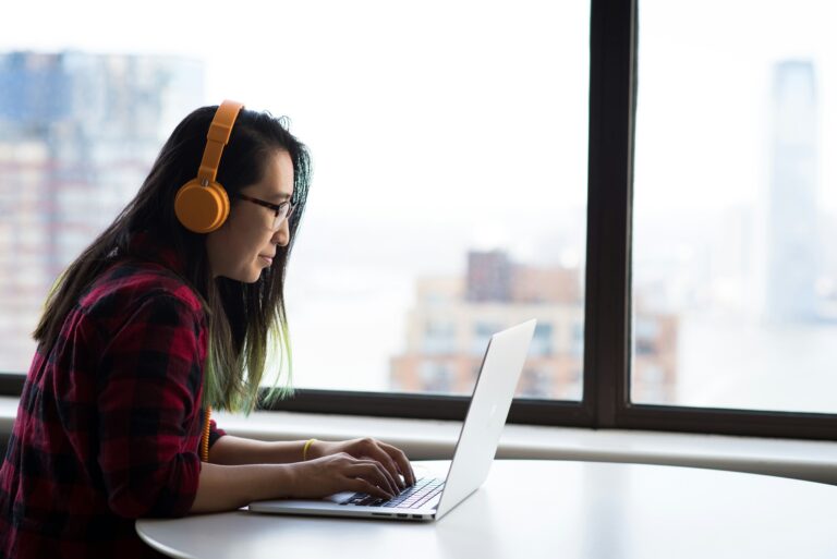 An individual sitting by a large window, working on their computer with headphones on. Want to know why continuing education is so important for therapists? Read insights in our blog!