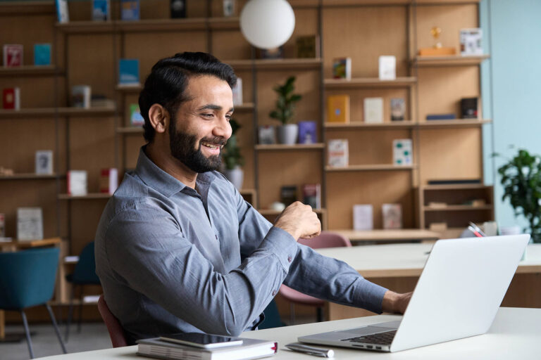 A professional smiling at his laptop while sitting at his desk. Representing how our continuing education for therapists can be done online! Get started with our professional development courses today.