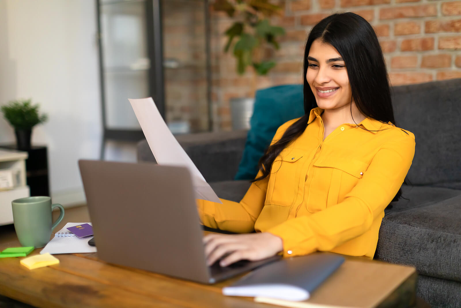 professional on laptop | ceus for marriage and family therapists | therapist ceu | ceus for therapists | New York | Vermont | Michigan A professional woman wearing a yellow blouse is smiling at her computer while holding a sheet of paper. Representing how our interesting online continuing education for therapists is essential for social workers, counselors & more. Start your continuing education journey today!